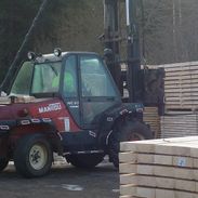 Traktors ar pacēlāju pie koka dēļu paletēm